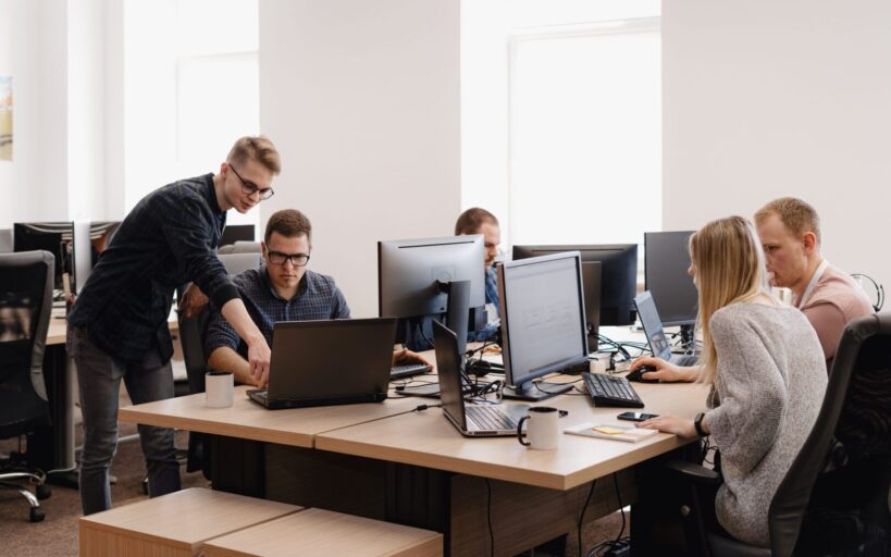 Full concentration at work. Group of young business people working and communicating while sitting at the office desk together with colleagues sitting in the background